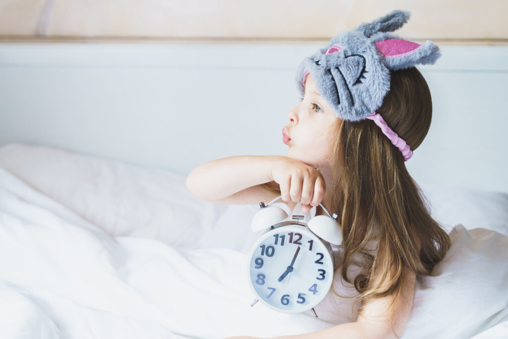 Mädchen mit Plüschschlafmaske und Wecker, Morgenroutine, Aufstehen für Kindergarten und Schule